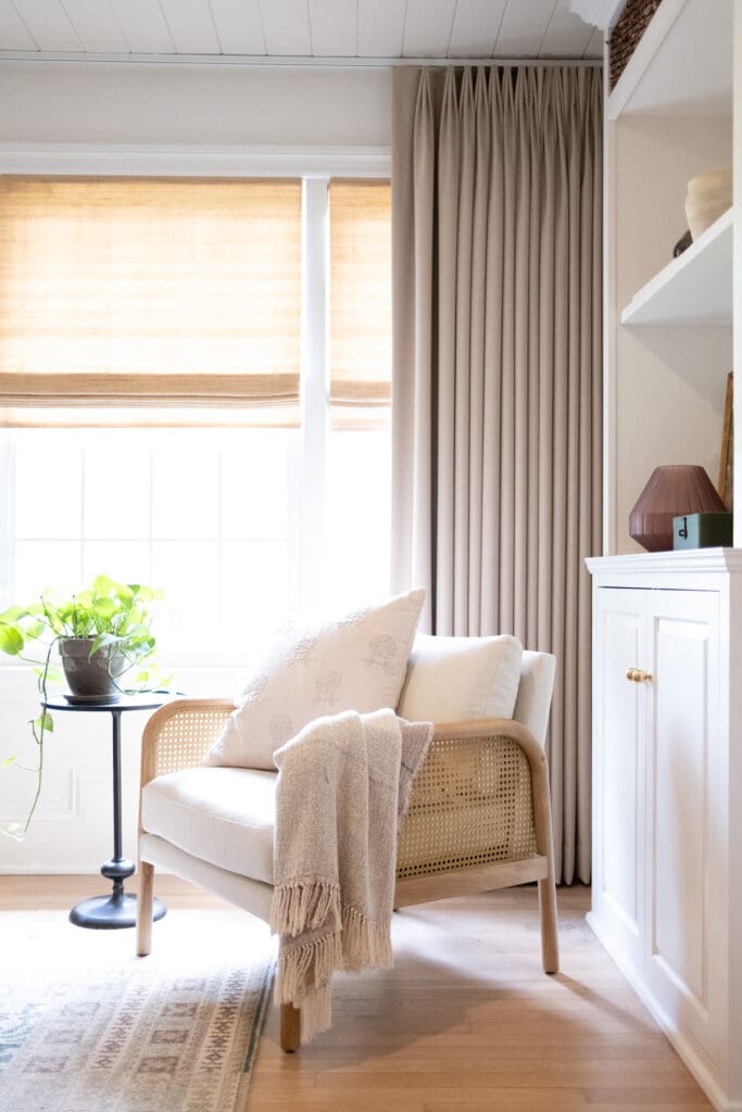 a cozy chair with rattan on the arms, placed in front of a window, in neutral colors, with light flowing in from the window
