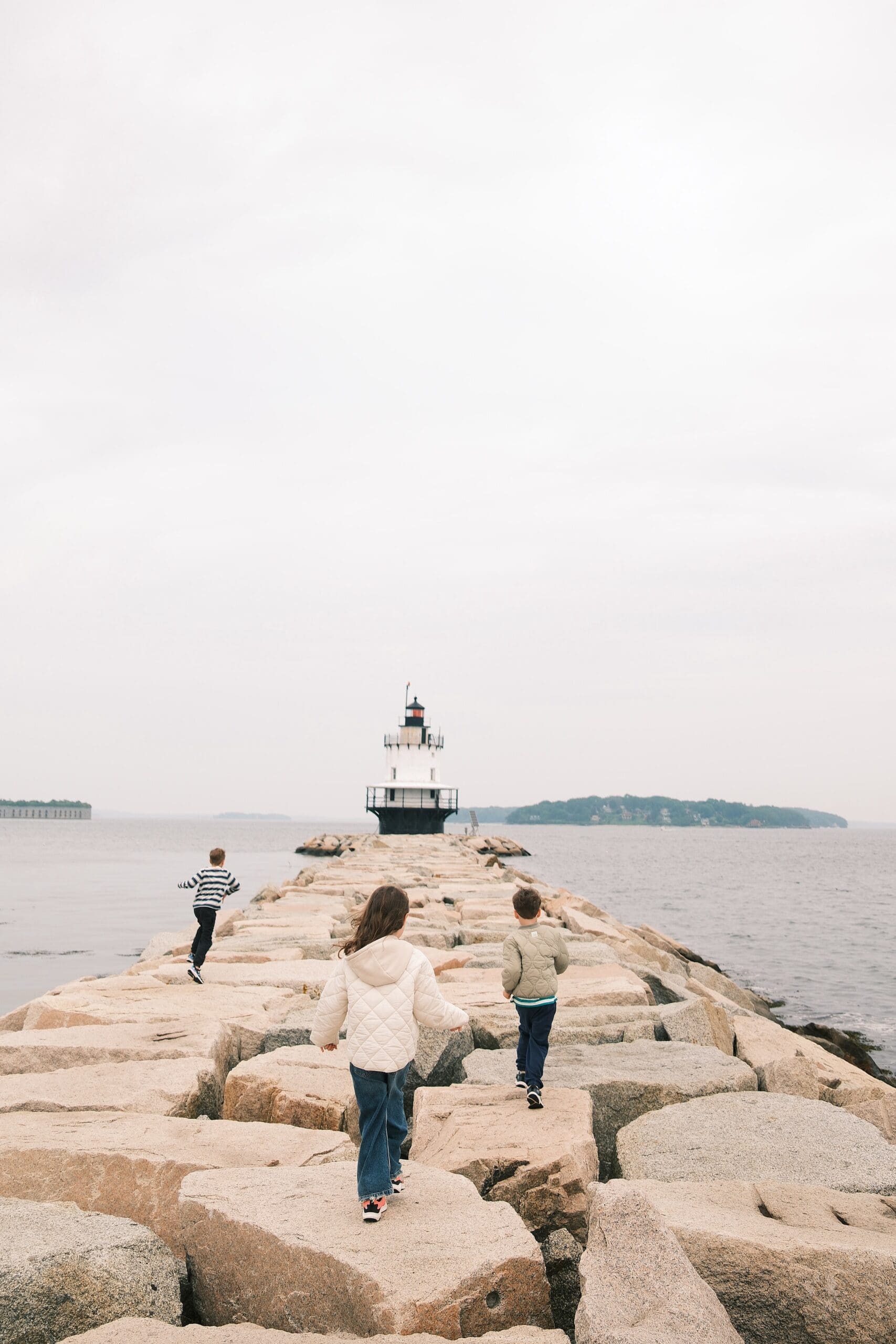 kids running towards a lighthouse that is in front of them in the distance, Portland Maine